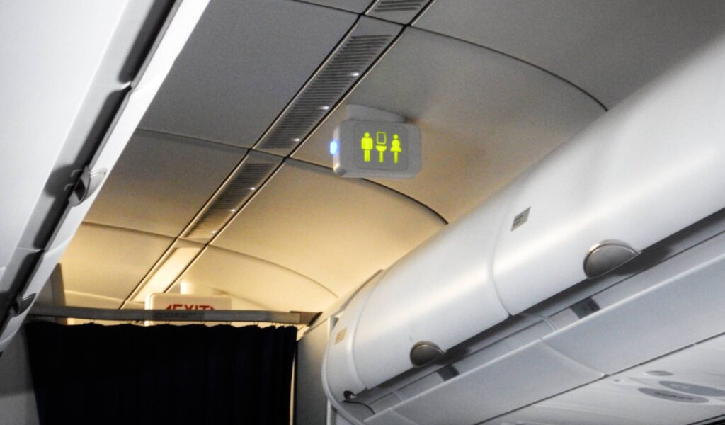 Accessible Bathrooms on Planes. When flying with a disability, what are your bathroom options? This image shows illuminated bathroom signs on an airplane. There are male, female, and accessible bathroom signs.