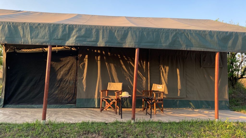 A large canvas safari tent set in the remote Serengeti, with a shaded porch supported by wooden poles. Two camping chairs and a small table sit in front of the tent. While the camp was relatively accessible for Laura and her friend, there were no accessible toilets available at this location.