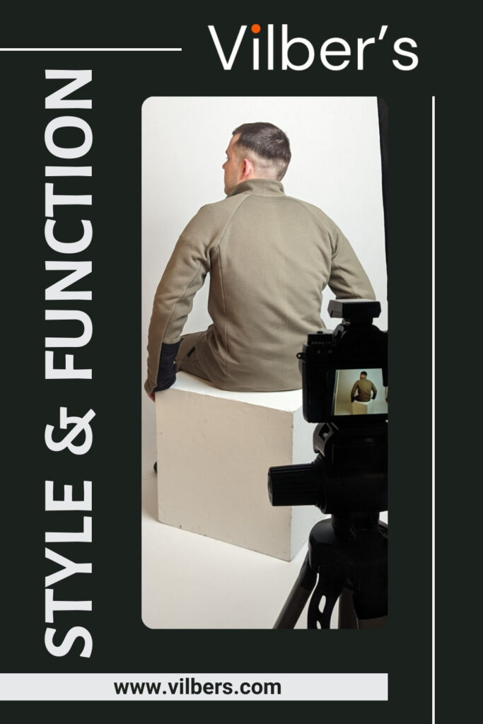 [Image Description: A promotional advert for Vilber's Adaptive, featuring a man sitting on a white block, facing away from the camera. He is wearing an olive-green jacket, showcasing the back of the adaptive clothing. A camera is positioned in front of him, capturing the scene. The words 'STYLE & FUNCTION' are written vertically on the left side of the image, and the Vilber's logo is at the top. At the bottom of the image is the website address: www.vilbers.com.]