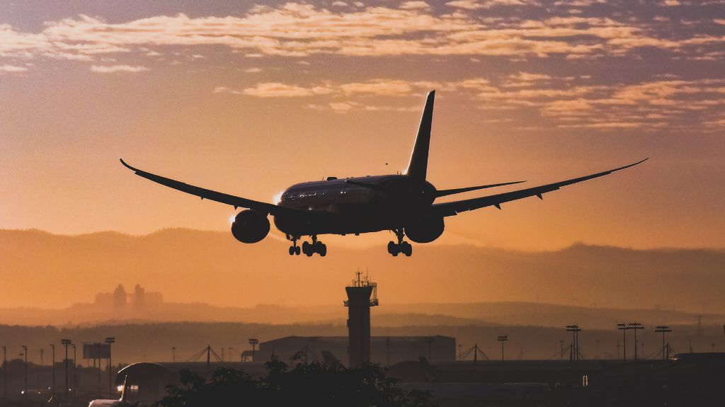 The outline of an aircraft coming into land with a sunset glow behind it.