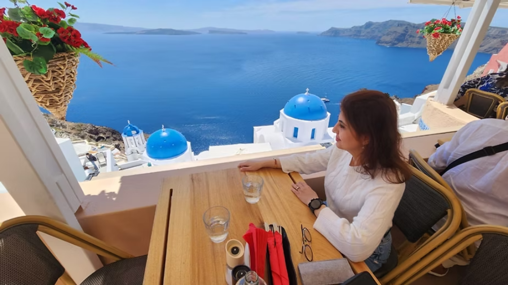 A woman enjoys a scenic oceanfront view of Santorini, Greece, from an accessible restaurant terrace with a clear view of blue-domed churches and the caldera.