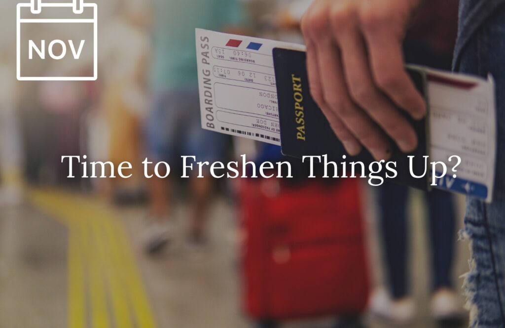 A close-up of a person holding a passport and boarding pass at an airport, with a blurred background of travelers and a red suitcase. Overlaid text reads “Time to Freshen Things Up?” and a calendar icon in the top left corner is marked “NOV,” suggesting a November travel theme or update.