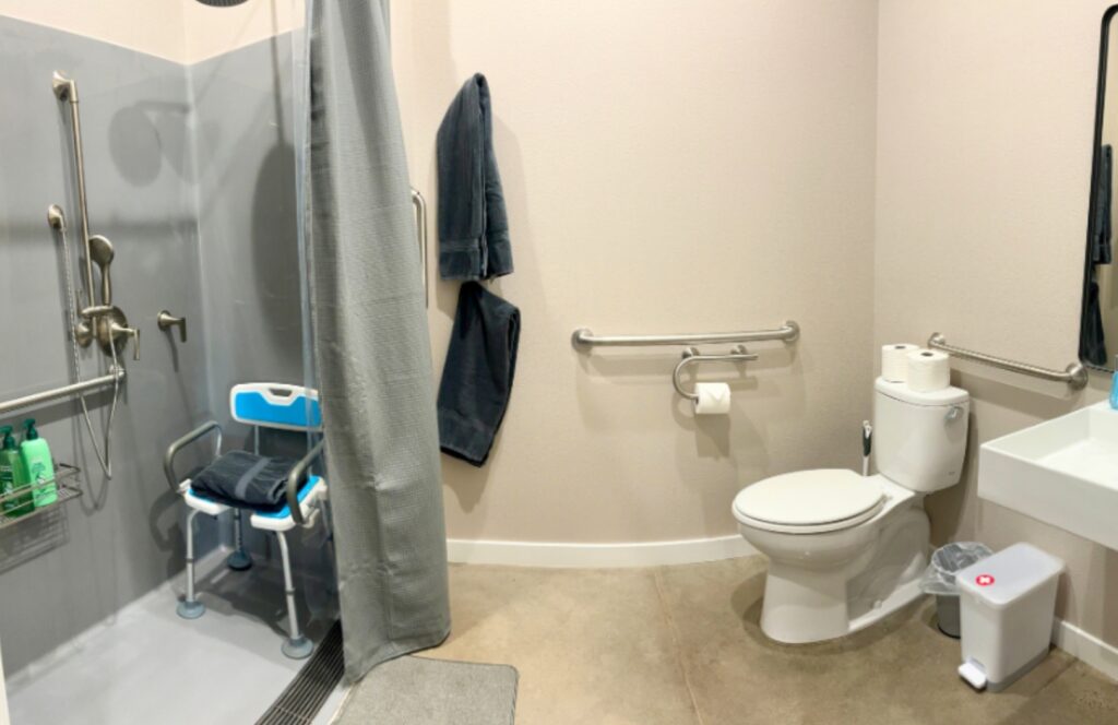 Fully accessible bathroom with roll-in shower, grab bars, raised toilet, roll-under sink, and height-adjustable shower chair at inclusive Yosemite vacation rental