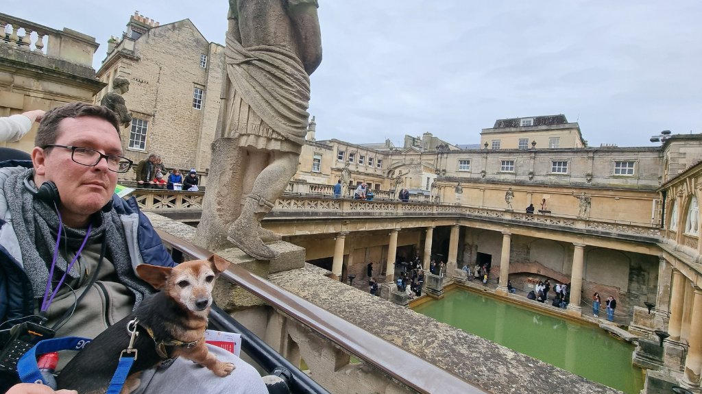 Shane in a wheelchair with his dog Jack at the Roman Baths in Bath, enjoying the accessible viewing platform overlooking the ancient site.