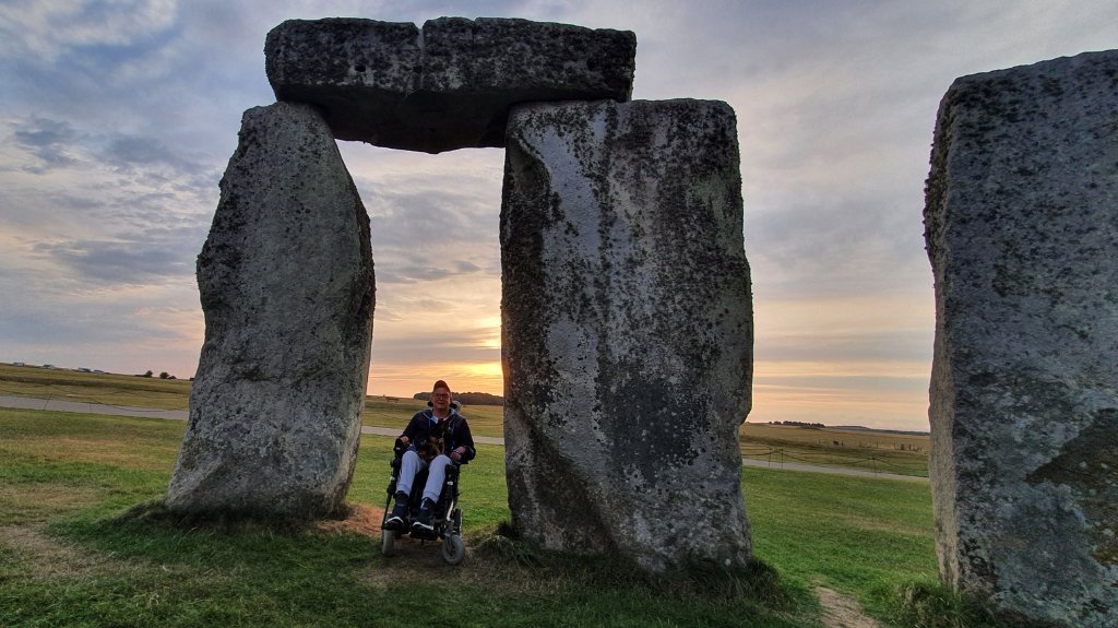 Shane sitting in his wheelchair between two of the stones at Stonehenge.