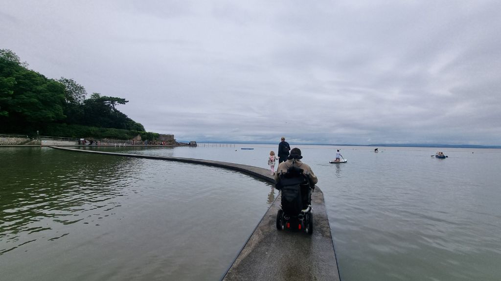 Shane in his wheelchair rolling along a thin path, slightly above the water, only visible and useable due to low tide.