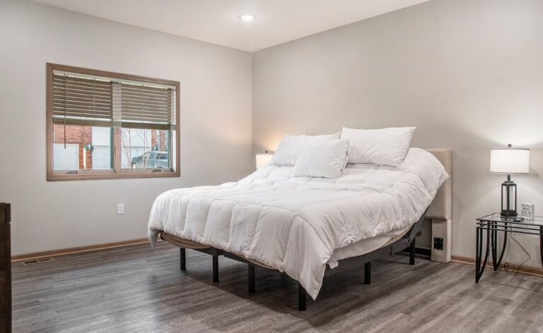 Modern bedroom with grey wood-style flooring and a large adjustable bed with a white comforter, allowing for customized head and foot elevation.