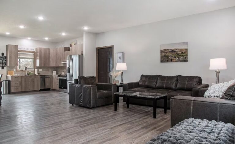 Comfortable living area with plush leather seating arranged around a large window, offering a view of the quiet residential neighborhood outside.