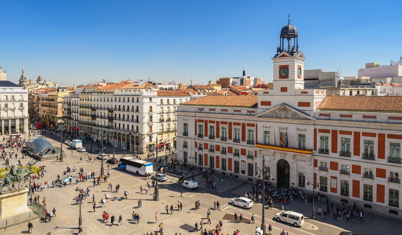 Aerial view of Puerta del Sol square in Madrid with the Real Casa de Correos clock tower and busy crowds below.