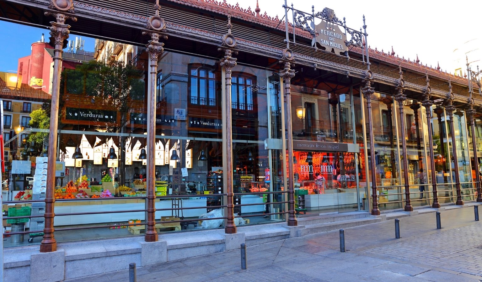 Glass and iron exterior of Mercado de San Miguel in Madrid showing fresh produce and food stalls inside.