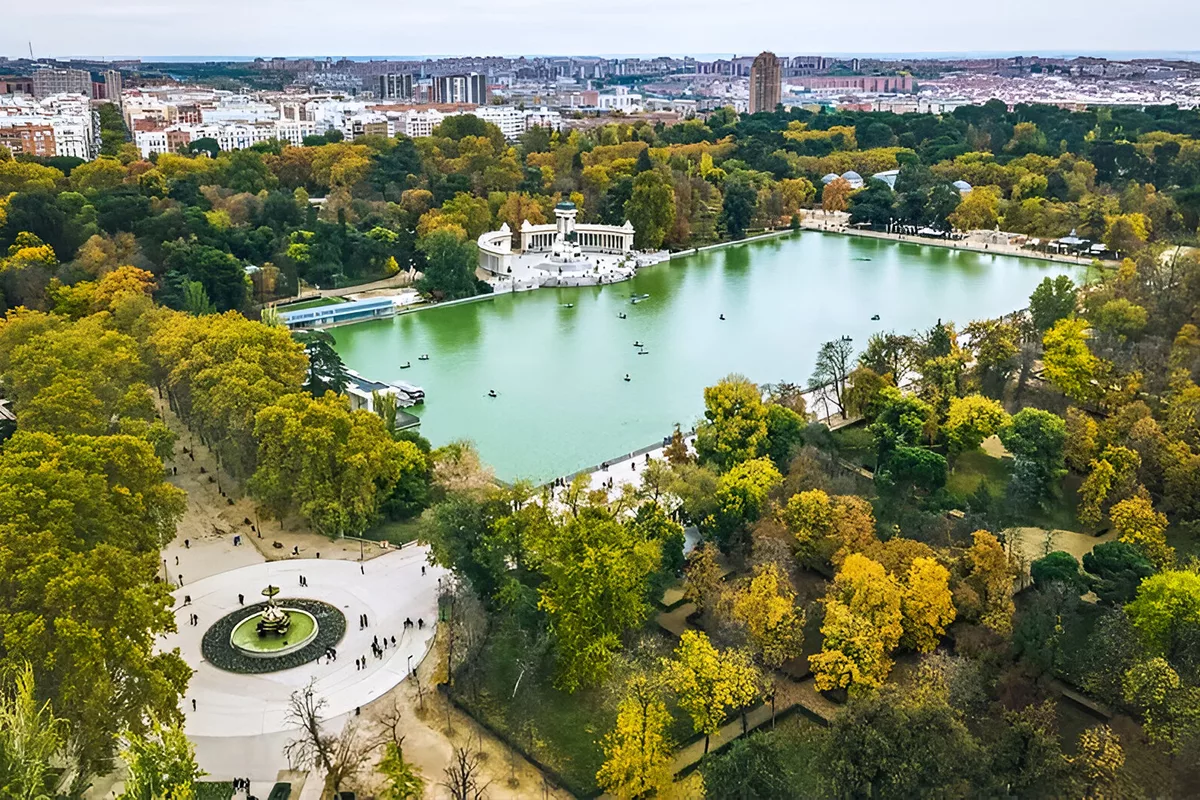 Aerial view of the Retiro Park Lake in Madrid with the Monument to Alfonso XII and surrounding autumn trees.