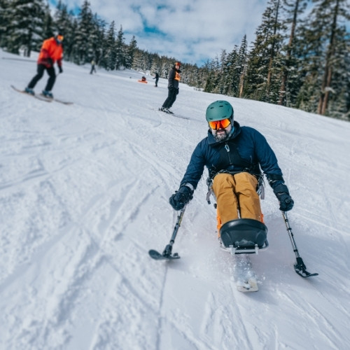 Person using adaptive ski equipment gliding down a snowy mountain slope, surrounded by other skiers.