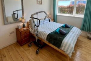 Accessible bedroom at Seahorses holiday bungalow in Brixham, with profiling bed, person hoist, and step-free wooden flooring.
