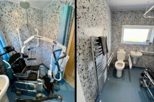Wheelchair-accessible wet room at Seahorses bungalow in Brixham, featuring tilt-in-space shower chair, hoist, grab rails, comfort-height toilet, and roll-under sink.