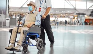 A man sits in a wheelchair and is pushed by an airport staff member. Meanwhile UK's Civil Aviation Authority propose new measures for avoiding wheelchair and mobility aid damages whilst flying.