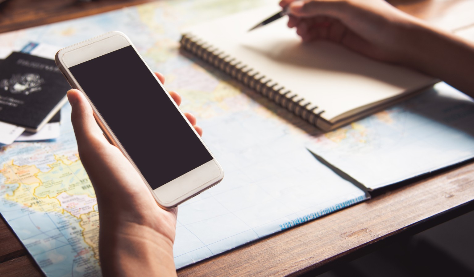 A person planning a trip at a wooden desk with a smartphone, open notebook, and world map, symbolizing how accessible travel agents help organize inclusive journeys for travelers with disabilities.