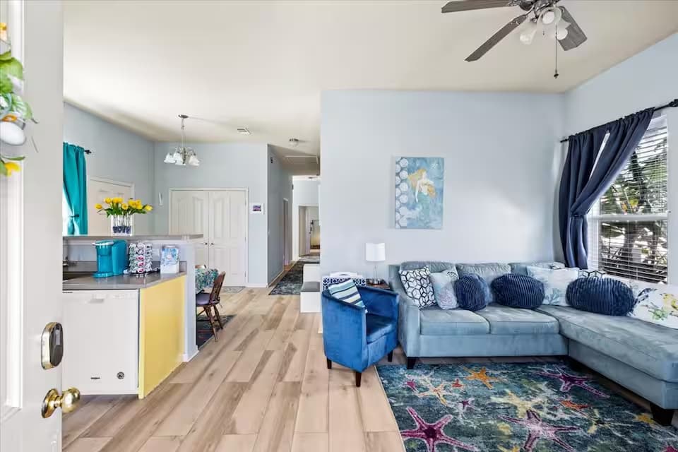 A wide-angle view from the front door looking into the living and dining areas. The space is bright and airy with light blue walls, high ceilings, and consistent wood-plank flooring throughout.