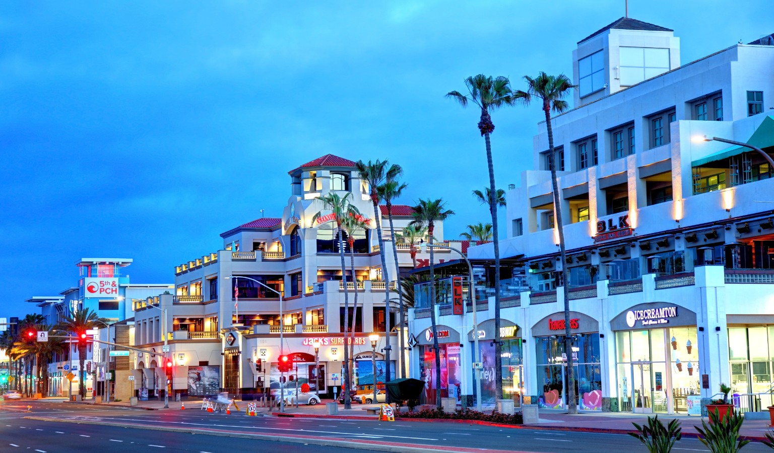 Evening view of downtown Huntington Beach, California, featuring palm-lined streets, bright shopfronts, and the 5th & PCH plaza near the oceanfront — a vibrant scene in one of the most wheelchair accessible beach towns in the USA.