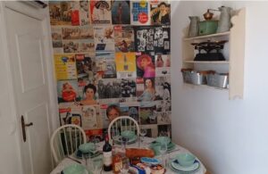 Table set with dinner plates bowls, cutlery and glasses, and in the background a wall covered in vintage art.