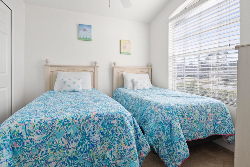 Bright and cheerful children's twin bedroom with two single beds dressed in colourful tropical-print quilts, polka dot cushions, playful wall art and a large sunlit window.
