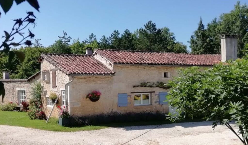 Exterior view of Maison des Renards, a traditional stone wheelchair accessible vacation property in Poitou-Charentes, France, surrounded by lush gardens under a clear blue sky.