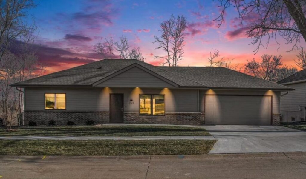 Front exterior of the Lemonade vacation rental at sunset, featuring a modern ranch-style house with gray siding, brick accents, warm outdoor lighting, and a spacious two-car garage.
