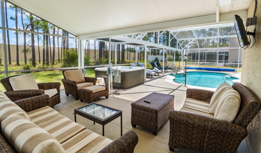 anai with large wicker sofa, armchairs and coffee tables overlooking a private outdoor pool and hot tub, with ceiling fan and wall-mounted TV. Sunloungers and a pool hoist are visible poolside.