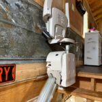 A view of the motorized chair lift from the top of the stairs, showing the lift unit at the landing level next to a white dresser.