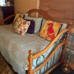 A cozy bed in the loft area featuring a colorful patchwork quilt with floral and geometric patterns, positioned against a rustic wood-paneled wall