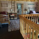 Interior view of the loft sleeping area featuring a bed with a floral patchwork quilt, a cowhide wall hanging, and a small wooden bedside table against wood-paneled walls.