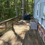 A spacious wooden wraparound deck with a sturdy railing, offering a clear, open path around the exterior of the cabin with views of the surrounding trees.