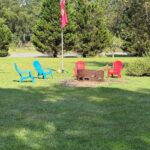 Outdoor seating area on the wooden deck featuring two high-back chairs facing a black circular fire pit, overlooking the forest.