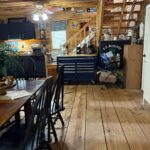 View of the kitchen area and wooden staircase. The stairs are equipped with a motorized chair lift, and the kitchen features dark cabinetry and a blue rolling tool chest used as a kitchen island.