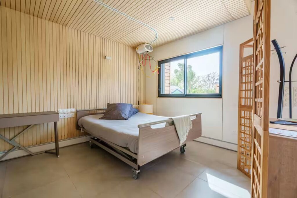 Accessible medical bedroom featuring an electric profiling double bed with a memory foam mattress and a ceiling-mounted rail hoist system for safe transfers.