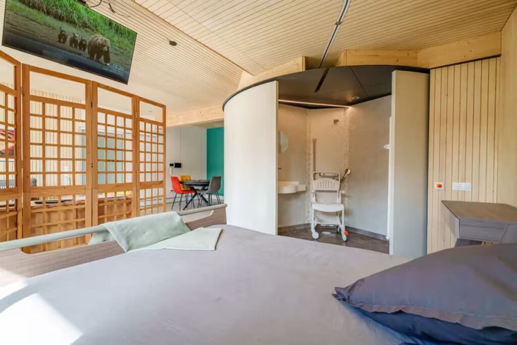 View from the medical bed showing the OTO system's accessible wet room, featuring a level-entry roll-in shower with non-slip flooring and integrated grab bars for safety.