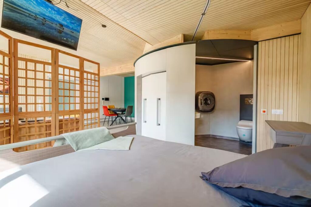 View from the medical bed of the OTO system's toilet area, featuring an accessible Japanese bidet toilet with sturdy wall-mounted grab bars on both sides.