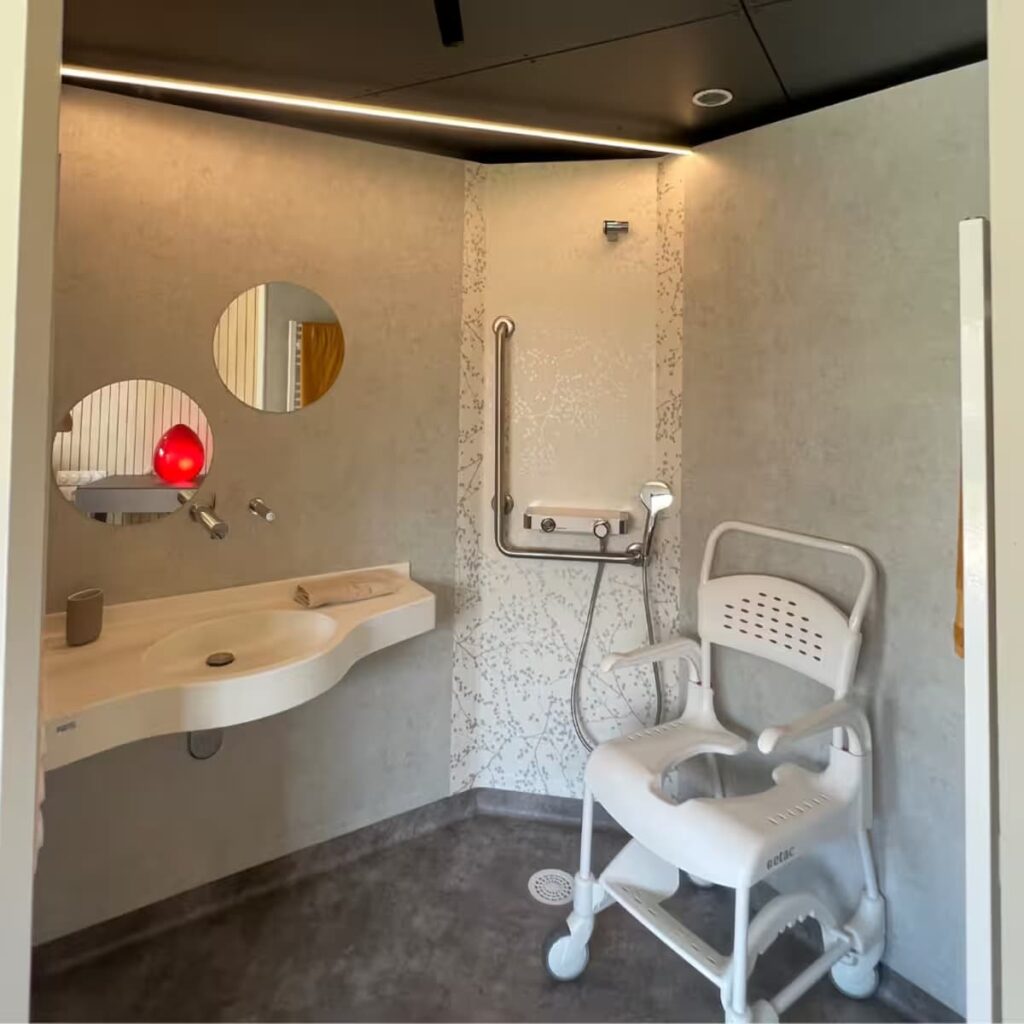 Walk-in roll-in shower area with non-slip flooring, integrated grab bars, and a Japanese-style bidet toilet, located within 2 meters of the bed.