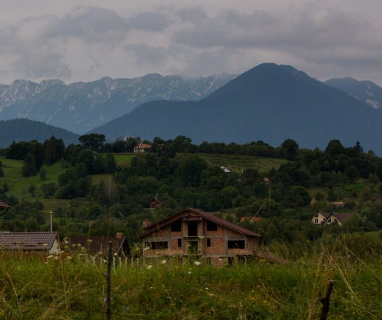 Rural village houses nestled among green hills and forests below the Carpathian Mountains near Brașov, Transylvania, Romania