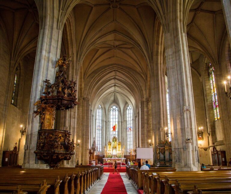 Interior of St. Michael's Church in Cluj-Napoca, Romania, showing Gothic vaulted ceilings, wooden pews and a red carpeted aisle leading to the altar