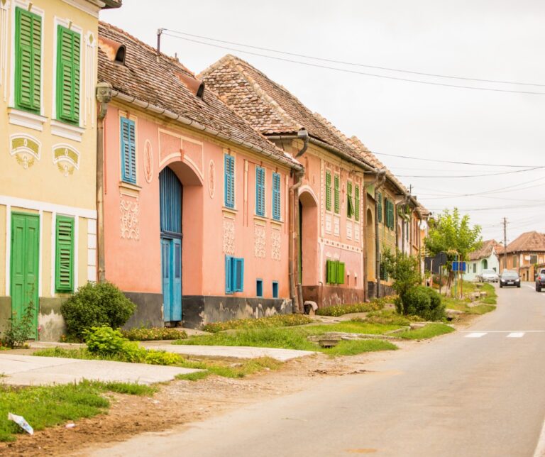 Row of colorful pastel-painted traditional village houses with wooden shutters lining a quiet road in rural Transylvania, Romania