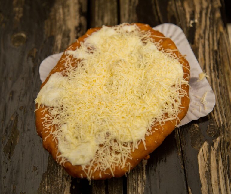 Lángos — traditional Eastern European fried dough topped with sour cream and grated cheese, served on paper at a street food stall in Romania