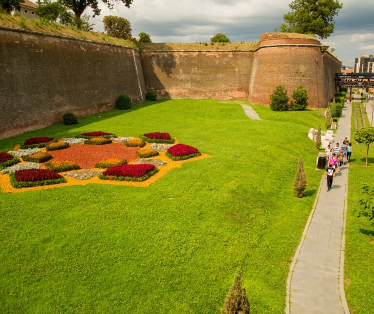 Ornate flower garden beside the restored brick fortress walls of Alba-Iulia citadel, Romania, with a smooth paved walkway alongside
