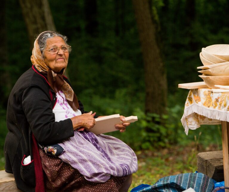 Elderly Romanian woman selling handmade wooden goods at a traditional craft fair at the Astra Open Air Museum, Sibiu, Romania