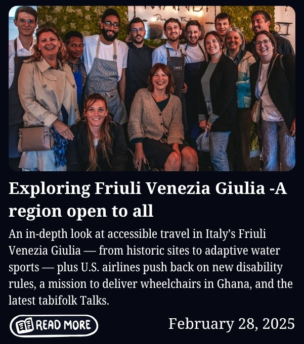 A group of around a dozen people pose together indoors in front of a green plant-covered wall, smiling at the camera. One woman sits in a wheelchair at the center, with others standing closely around her in a friendly, social setting. Below the image, text reads: “Exploring Friuli Venezia Giulia – A region open to all,” followed by a summary about accessible travel in Italy, disability travel news, a wheelchair delivery mission in Ghana, and tabifolk Talks, along with a “Read More” button and the date February 28, 2025.