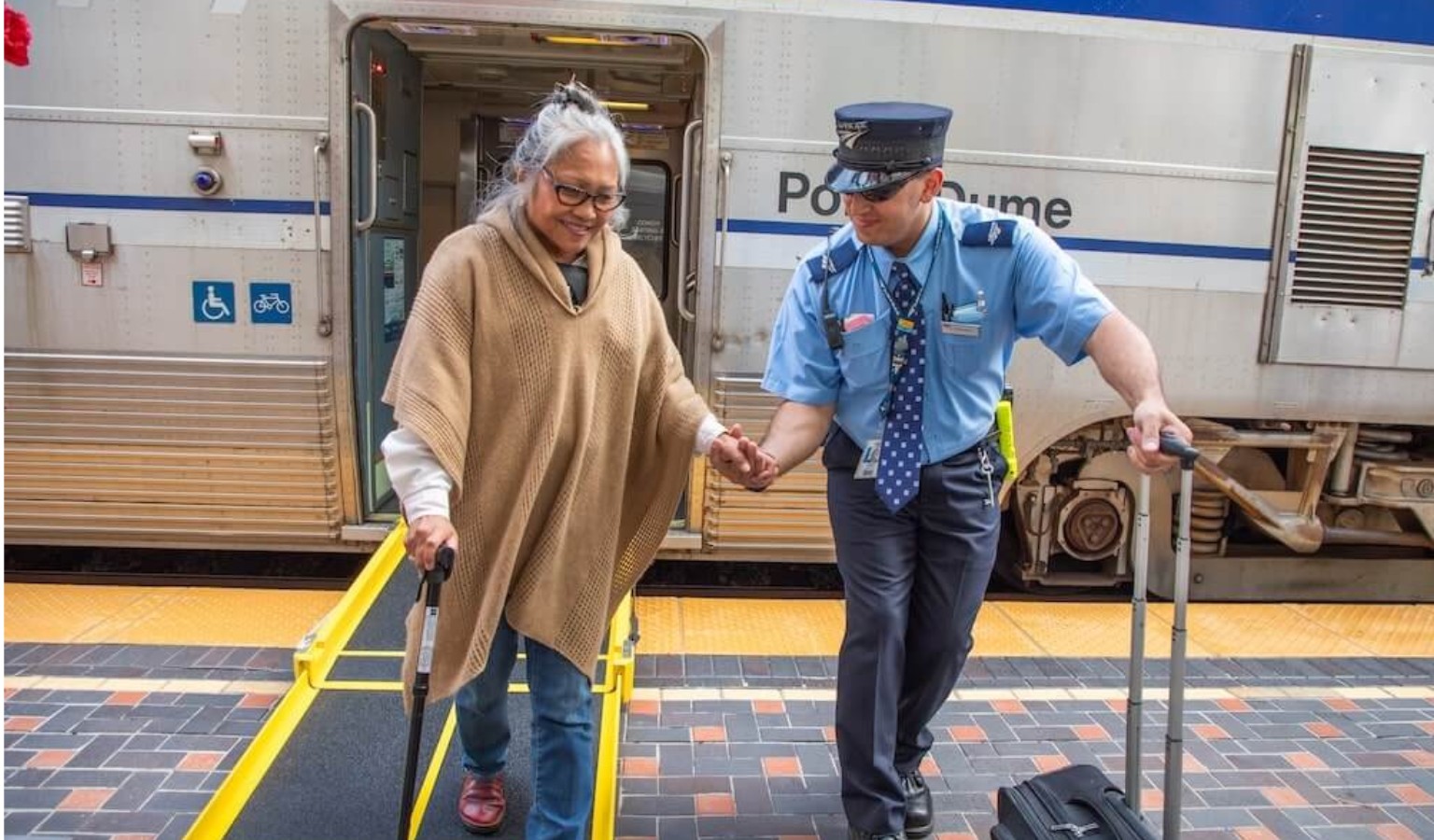 Train conductor helping an elderly woman with a walking stick disembark via a accessibility ramp at a Los Angeles Metrolink station – accessible transport in LA