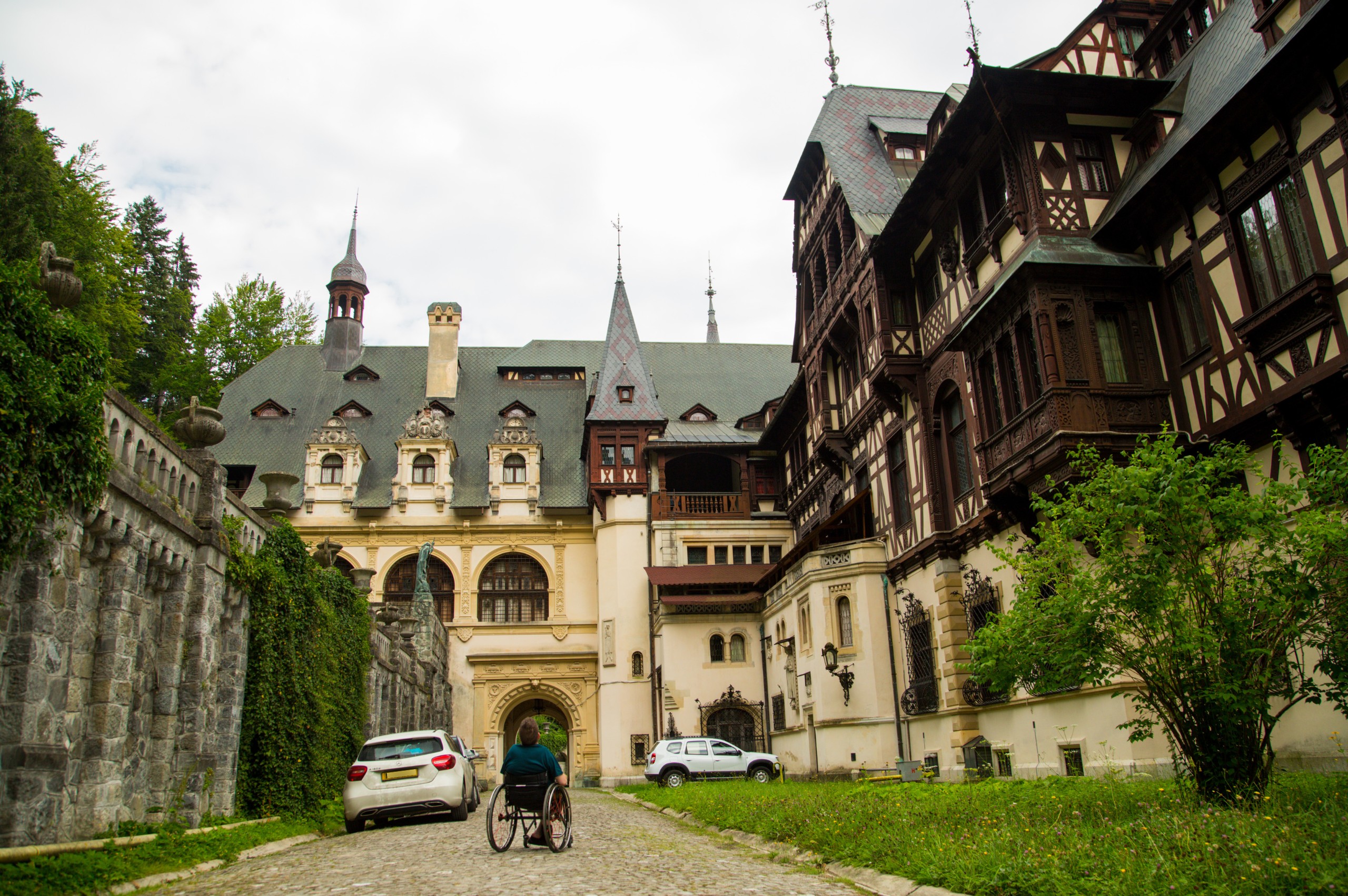 Wheelchair user approaching the entrance of Peleș Castle in Sinaia, Romania, along a cobblestone path through the private estate