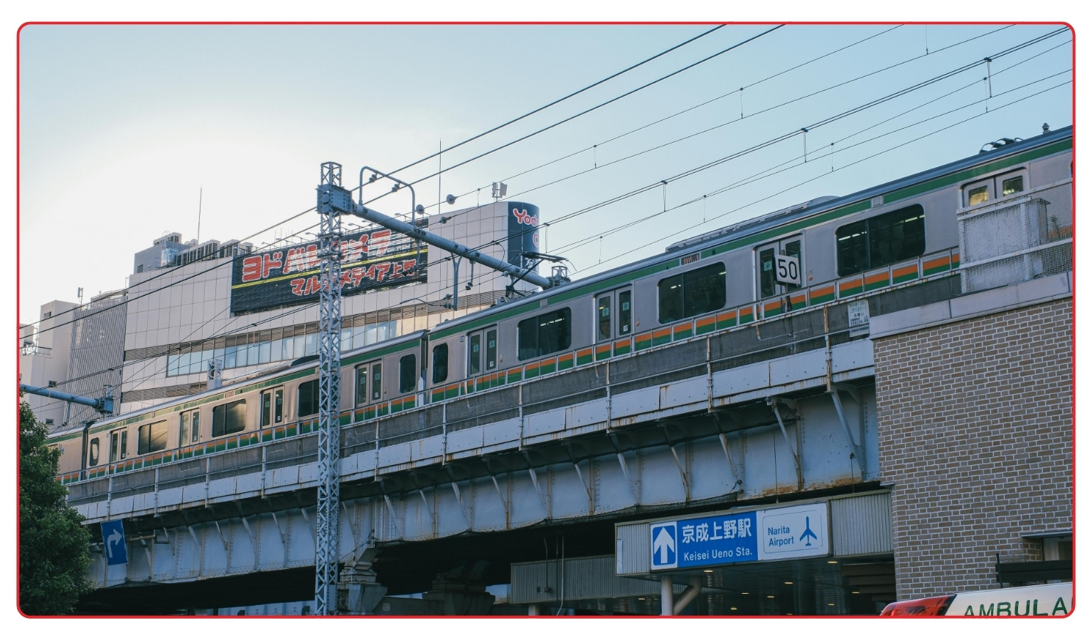 A JR train on an elevated track near Ueno Station in Tokyo, with a road sign below pointing to Keisei Ueno Station and Narita Airport