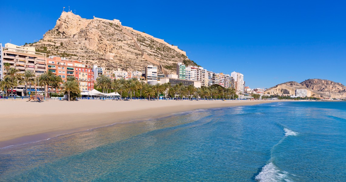 Postiguet Beach in Alicante with Castillo de Santa Bárbara rising above the city, home to Alicante's accessible beach program